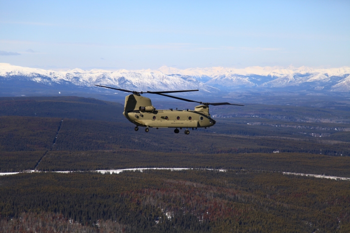 CH-47F Chinook helicopter 10-08083 flies along the Alaska Canada Highway (ALCAN) north of Fort St. John, British Columbia. In the background is the northern end of the Rocky Mountains.
